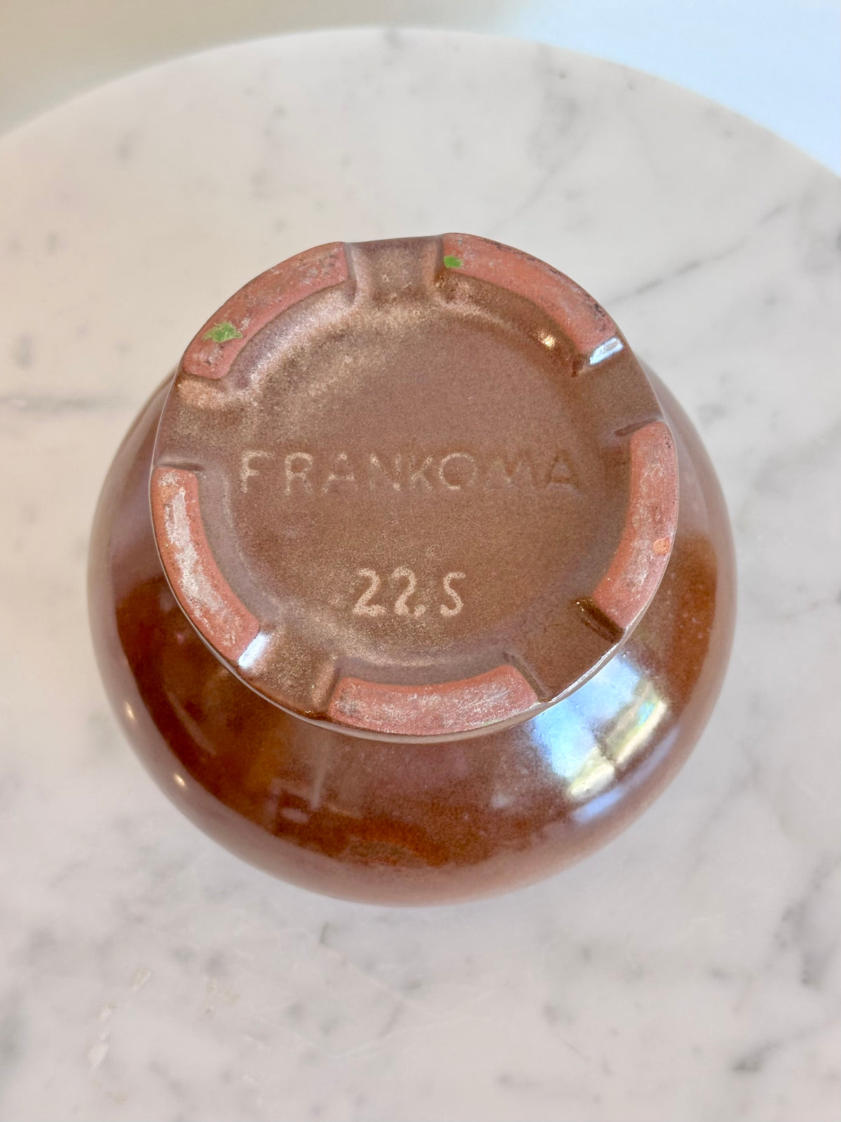 Top-down view of a brown ceramic bowl or vase with a glossy finish, showing the embossed brand name 'FRANKOMA' and the code '22.S' on the bottom, resting on a white marble surface., photo 6