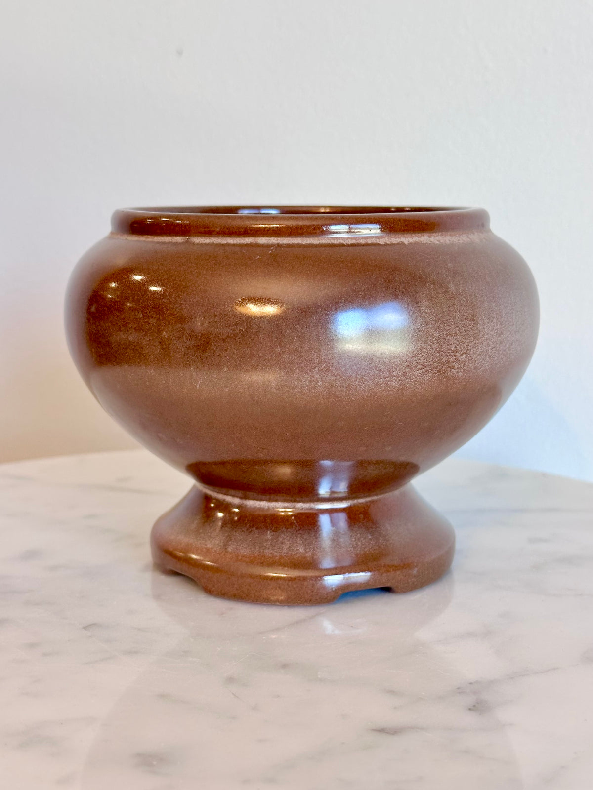 A small round ceramic planter pot with a  brown and bronze glaze, sitting on a white marble surface against a plain white wall., photo 4