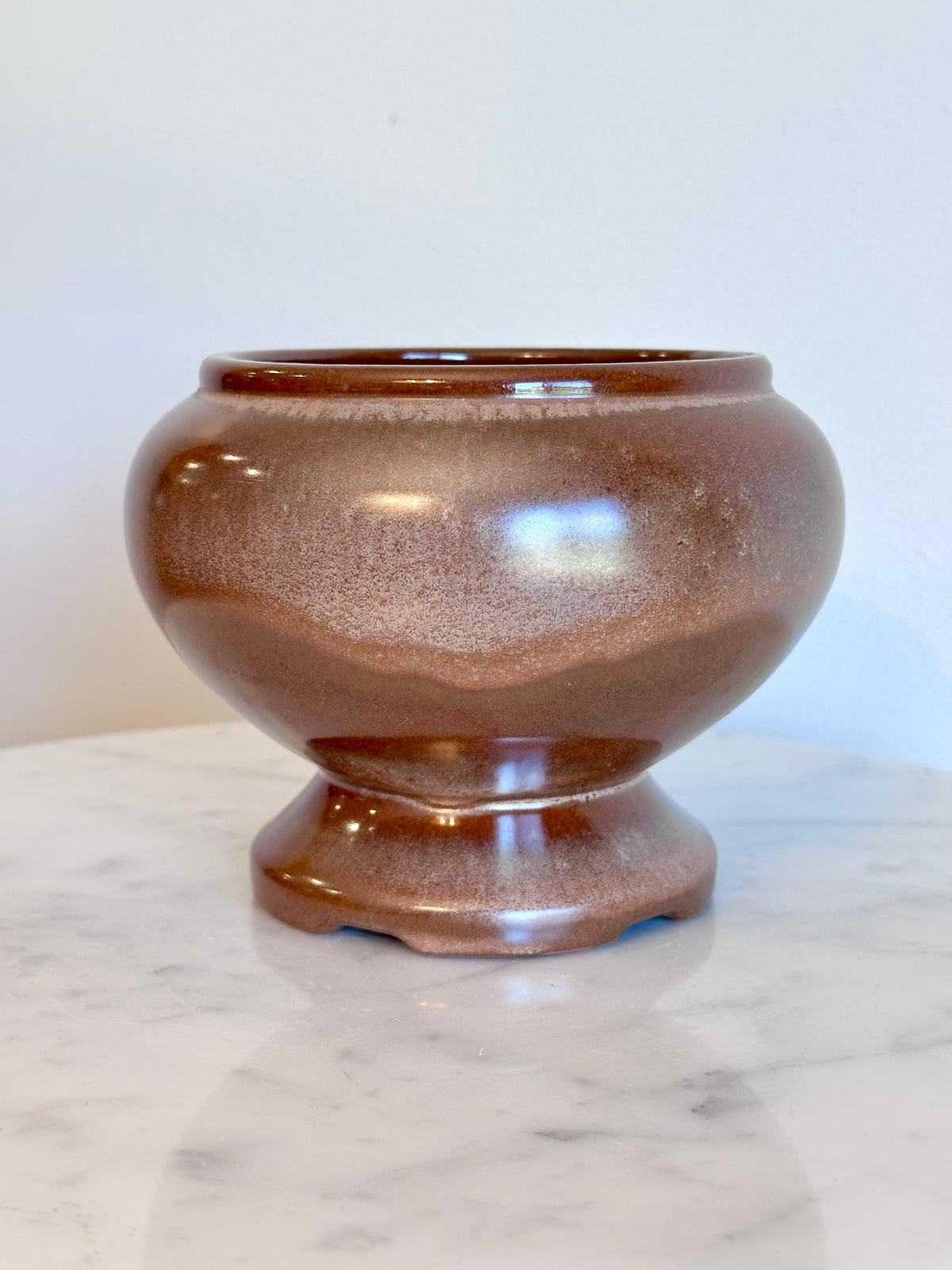 A small round ceramic planter pot with a  brown and bronze glaze, sitting on a white marble surface against a plain white wall., photo 2