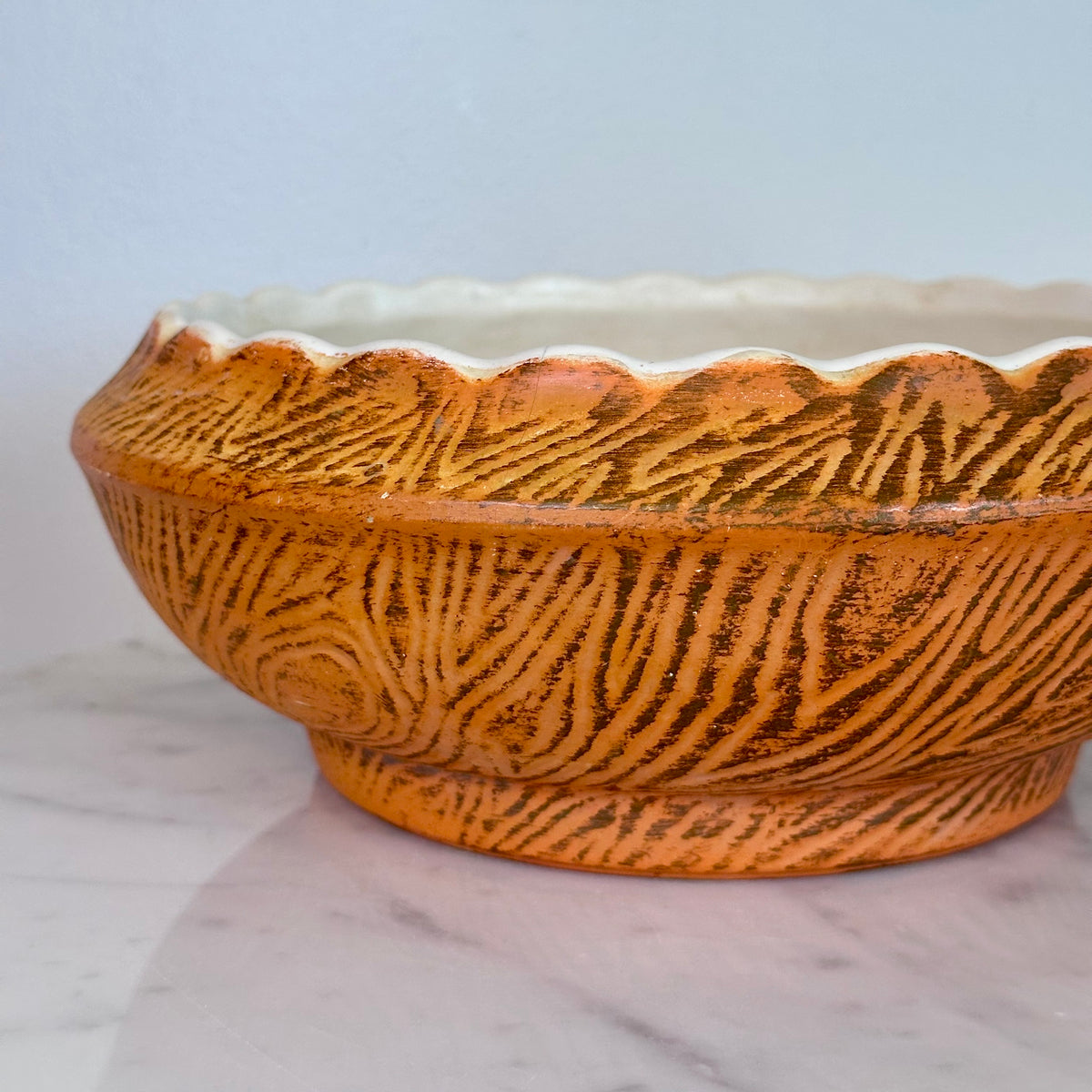 A close-up of a ceramic bowl with a textured, hand-painted orange and brown pattern, featuring a scalloped rim and a white interior, set on a light marble surface., photo 3
