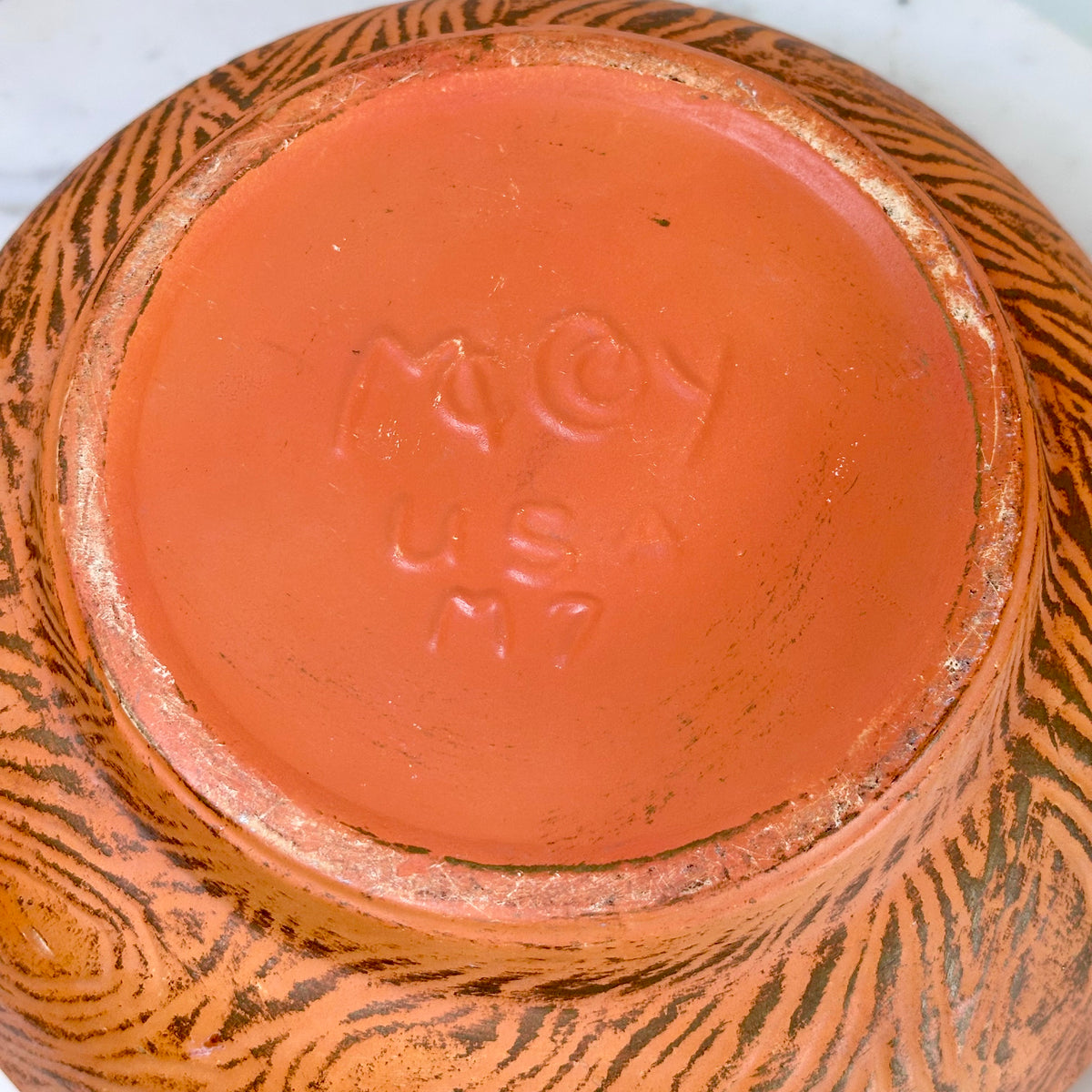 Close-up of the bottom of a ceramic pot or vase, showing a terracotta-colored foot ring with embossed maker's mark text and a brown tree bark patterned glaze around the exterior., photo 8