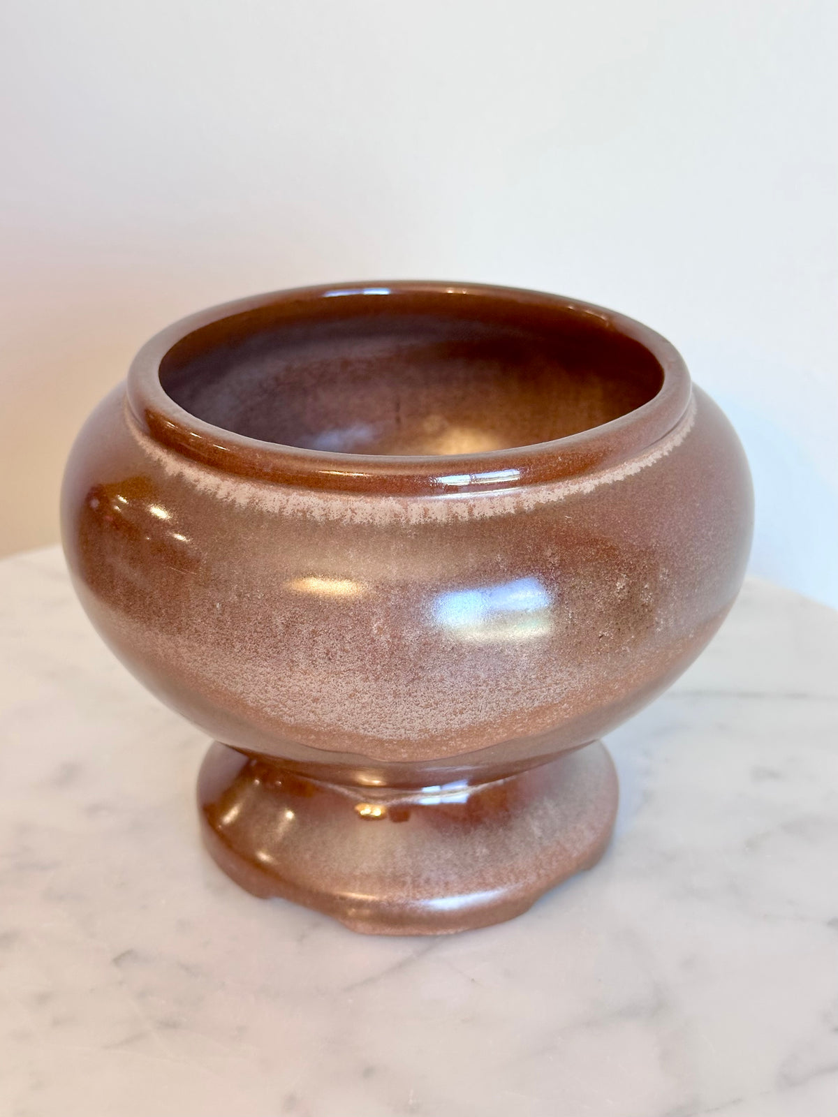 A small round ceramic planter pot with a  brown and bronze glaze, sitting on a white marble surface against a plain white wall., photo 3