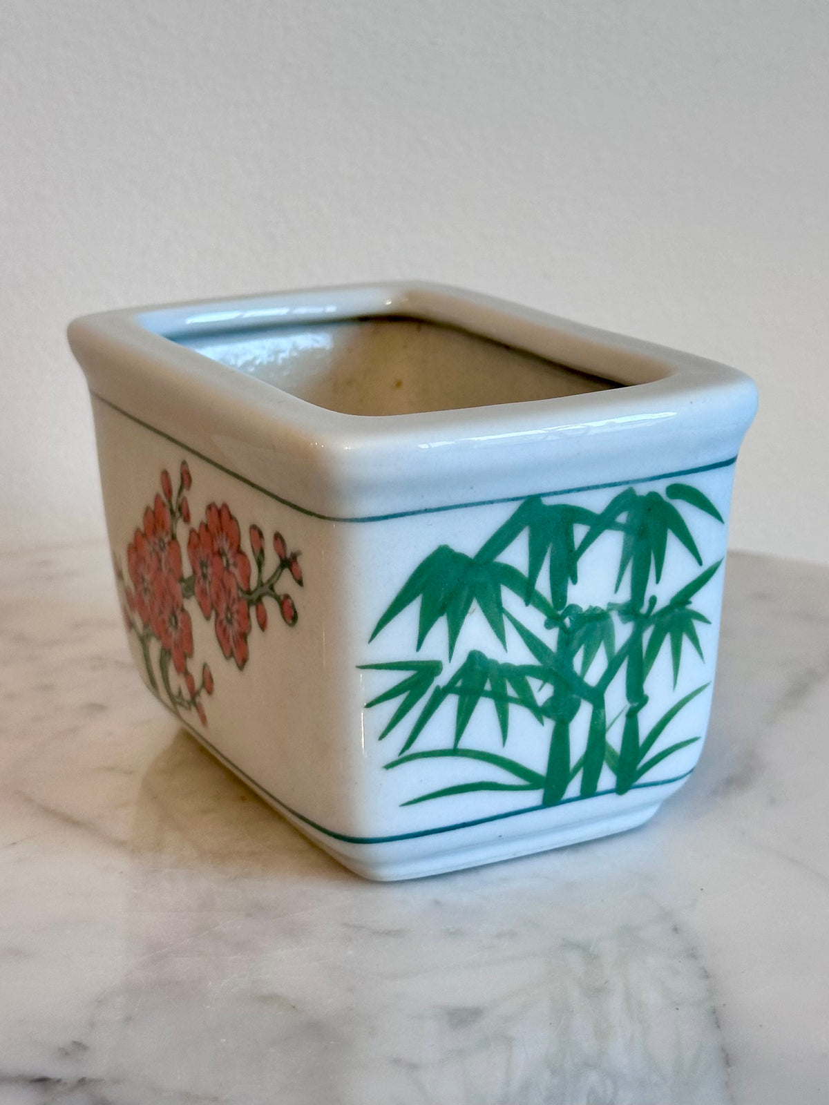 A square white ceramic planter with rounded corners, decorated with green bamboo and red flowers, sitting on a white marble surface against a neutral beige background., photo 3