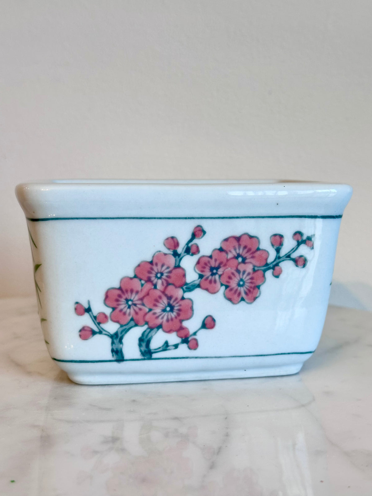 A small rectangular white ceramic planter or vase with a hand-painted pink floral branch design on the side, resting on a light marble surface against a plain light background., photo 2