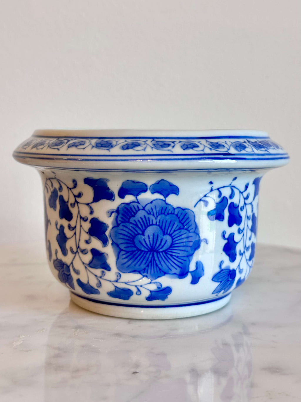A classic blue and white porcelain planter with a floral pattern, sitting on a white marble surface against a plain off-white wall.