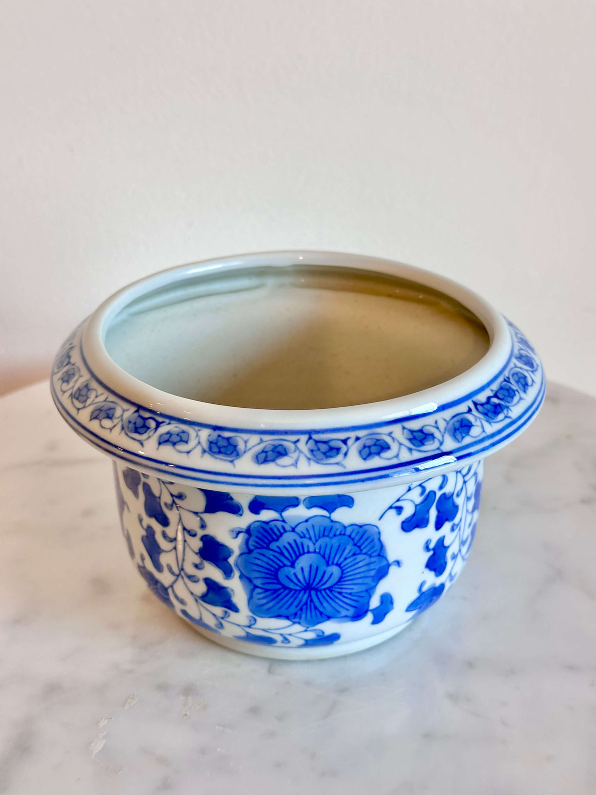 A classic blue and white porcelain planter with a floral pattern, sitting on a white marble surface against a plain off-white wall.
