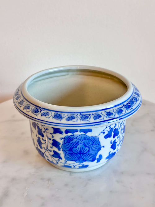 A classic blue and white porcelain planter with a floral pattern, sitting on a white marble surface against a plain off-white wall.