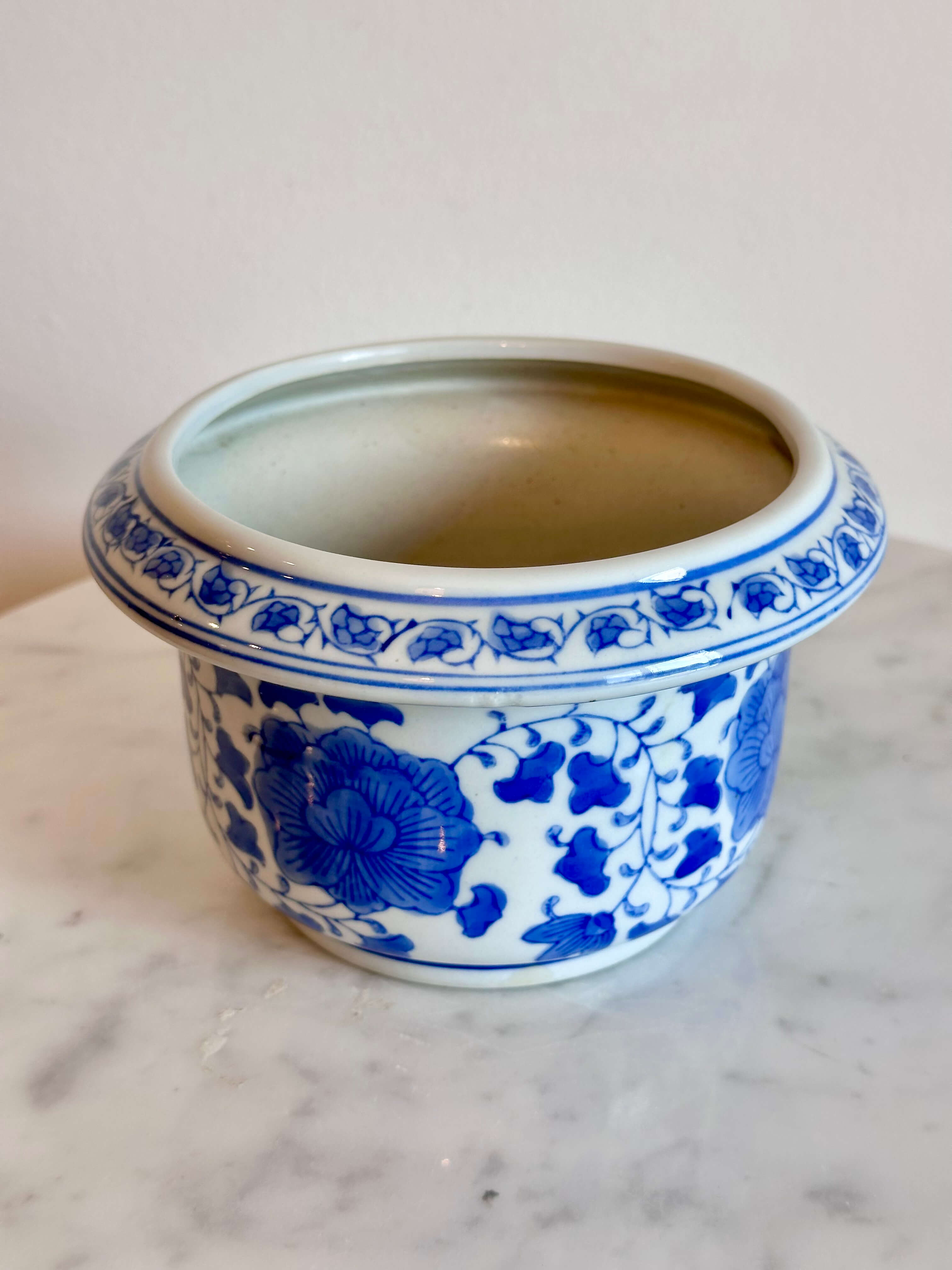 A classic blue and white porcelain planter with a floral pattern, sitting on a white marble surface against a plain off-white wall.