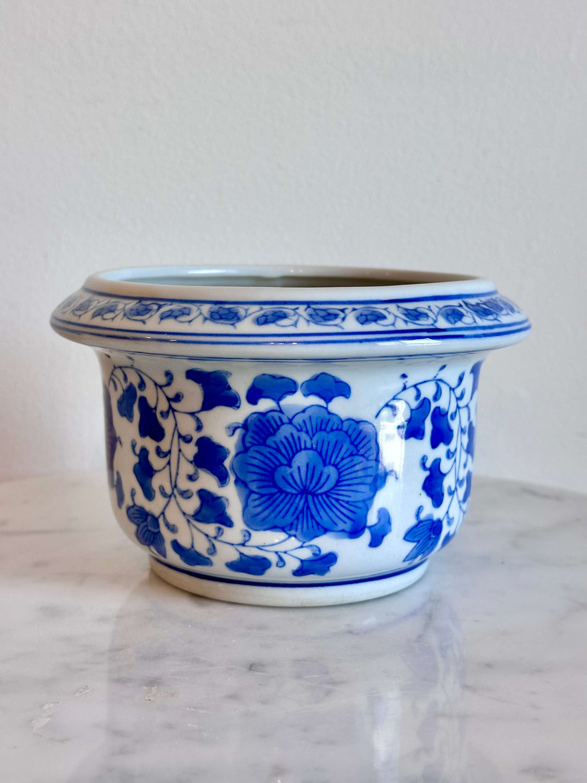 A classic blue and white porcelain planter with a floral pattern, sitting on a white marble surface against a plain off-white wall.