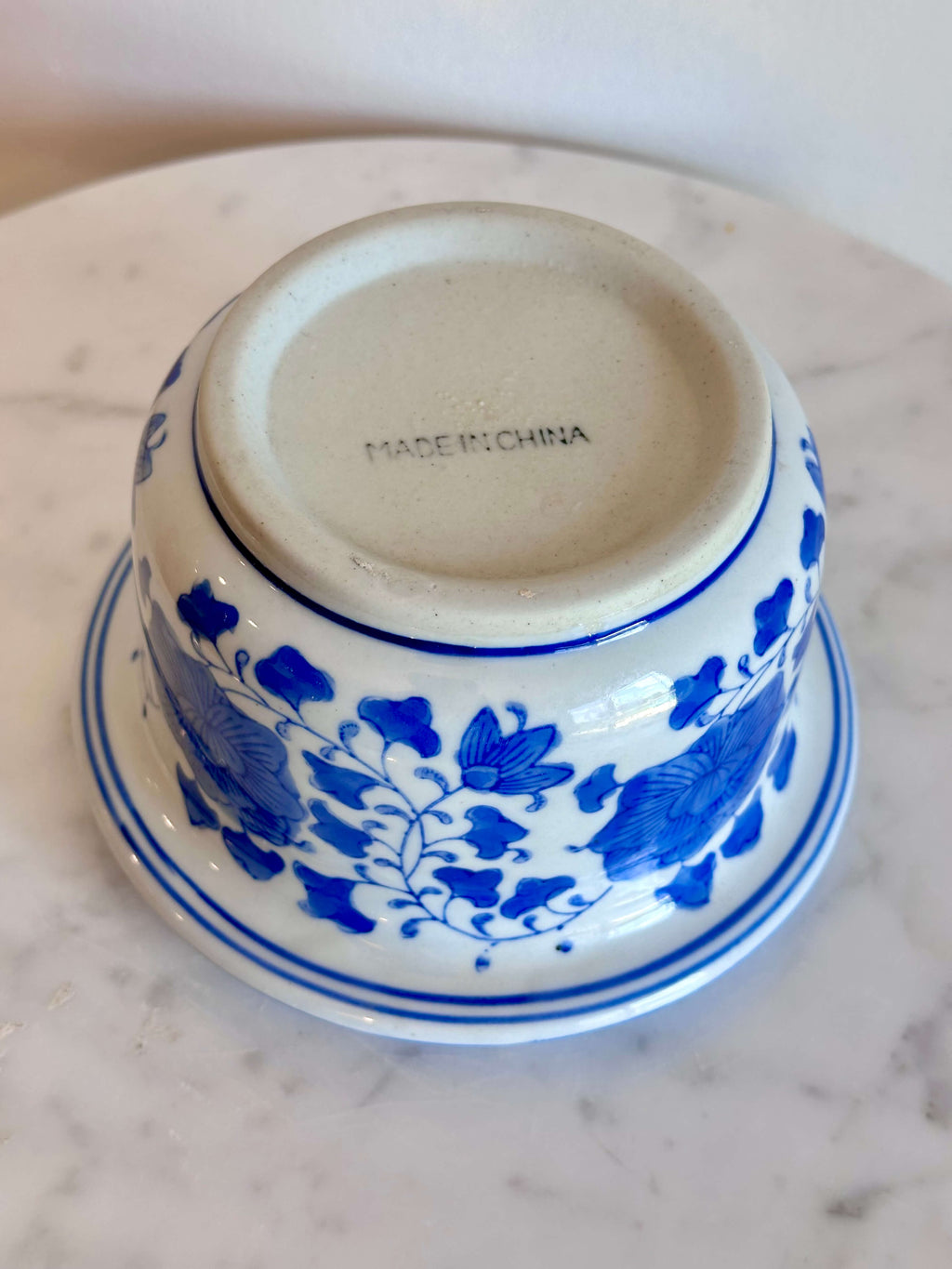 A classic blue and white porcelain planter with a floral pattern, sitting on a white marble surface against a plain off-white wall.