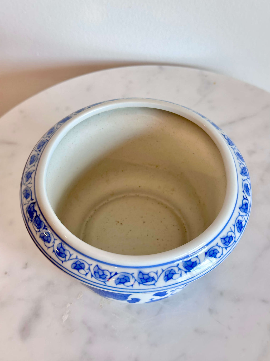 A classic blue and white porcelain planter with a floral pattern, sitting on a white marble surface against a plain off-white wall.