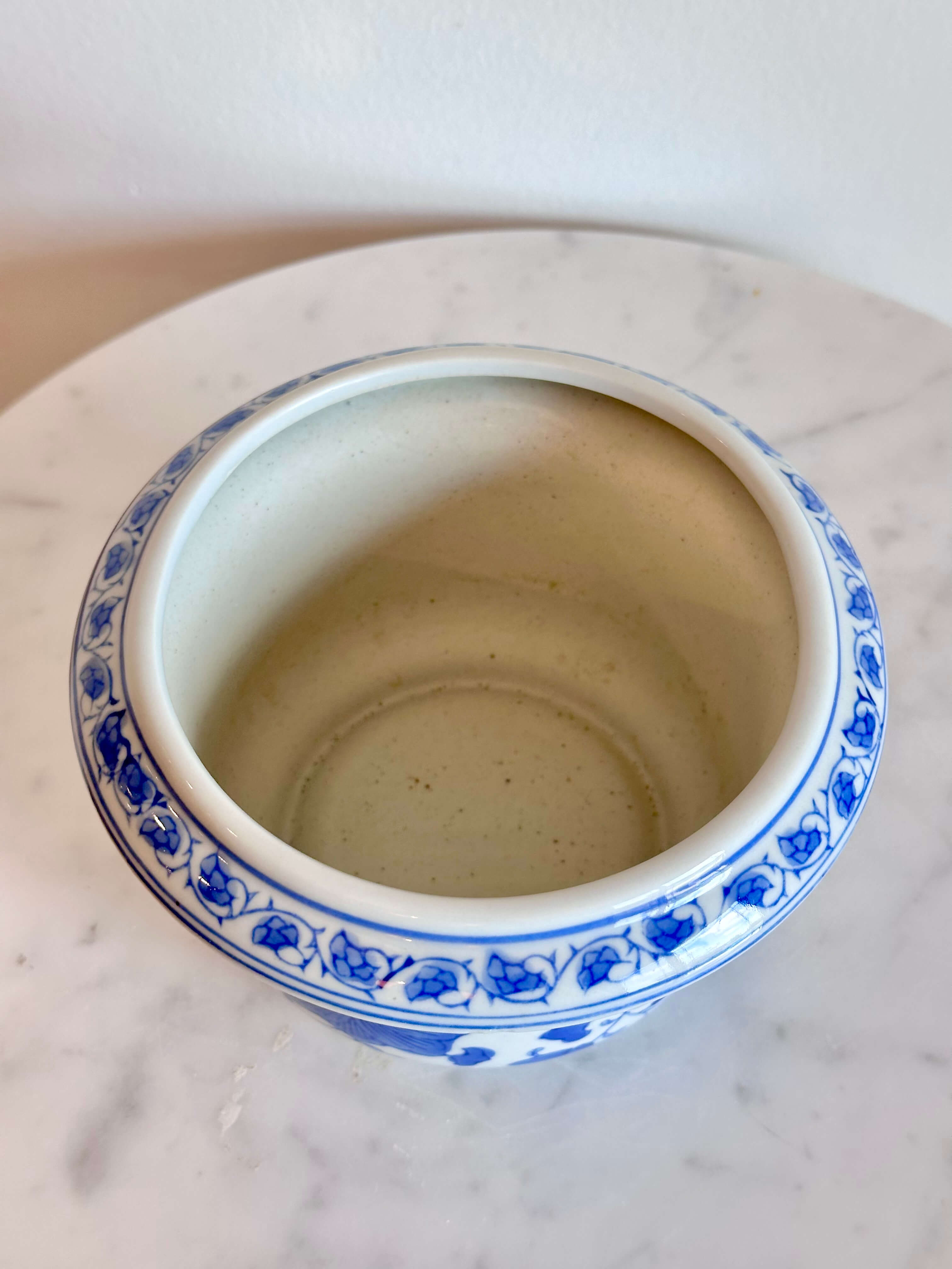A classic blue and white porcelain planter with a floral pattern, sitting on a white marble surface against a plain off-white wall.