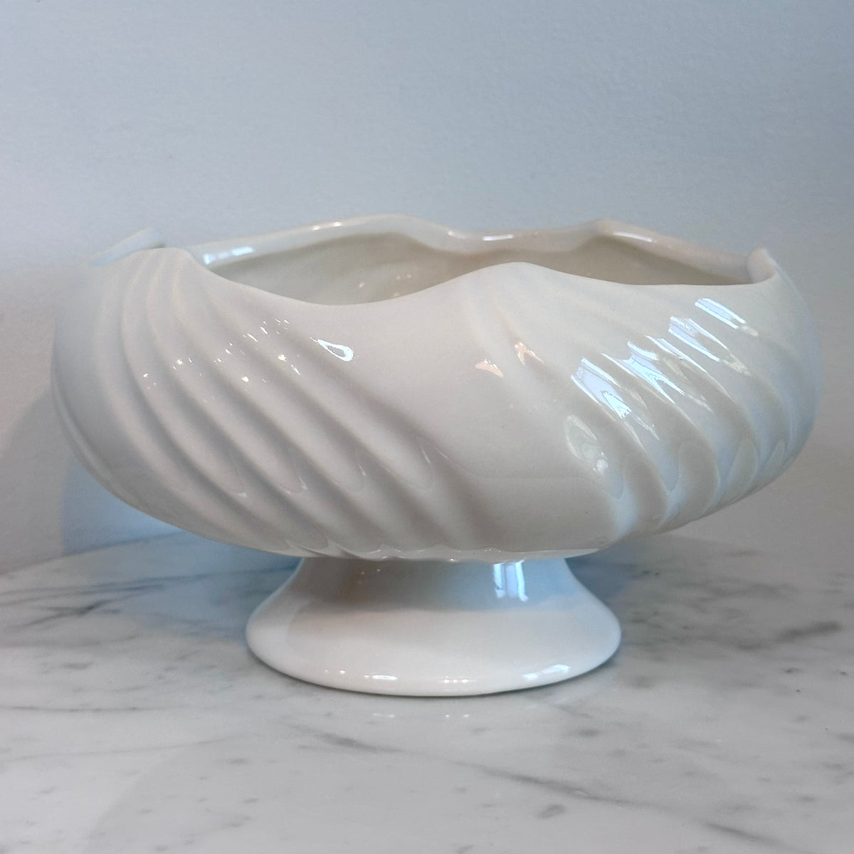 A glossy white ceramic pedestal bowl with a fluted, ribbed exterior and wavy rim, displayed on a white marble surface against a light gray background., photo 2
