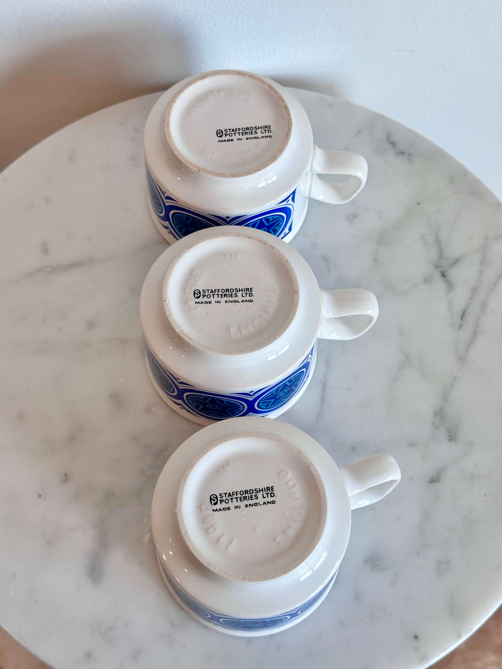 Three white ceramic Mugs with blue geometric patterns, shown upside down on a round white marble tray.