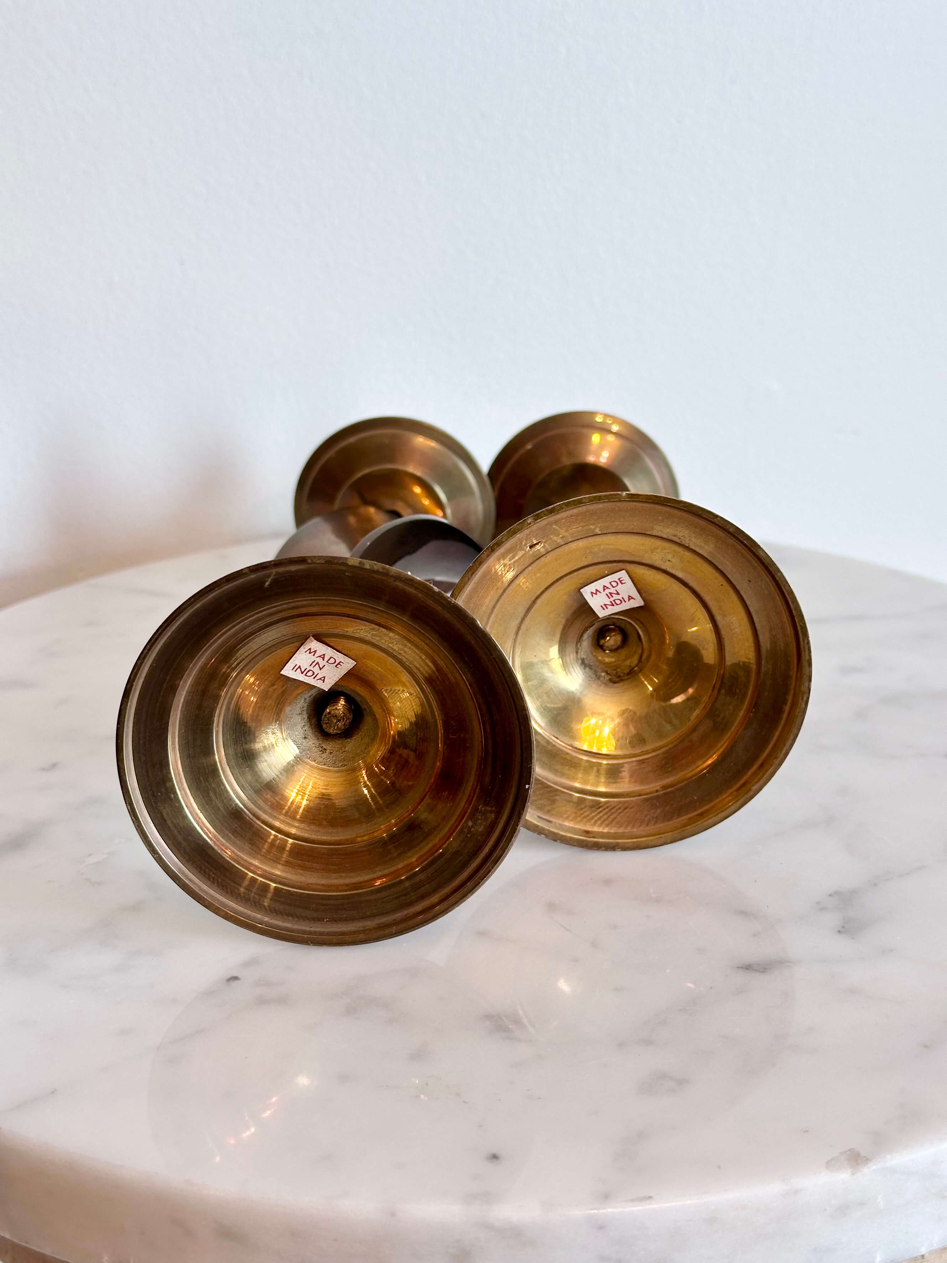 A pair of vintage brass spiral candlesticks with circular bases, displayed on a white marble surface against a white wall.
