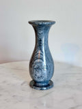 A small gray and white marbled stone vase with a flared rim and circular base, standing on a white marble surface against a plain off-white wall.