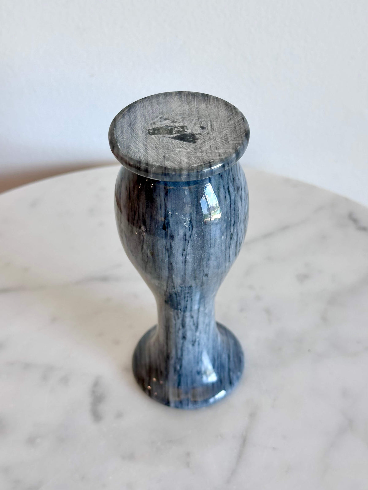 A small gray and white marbled stone vase with a flared rim and circular base, standing on a white marble surface against a plain off-white wall.