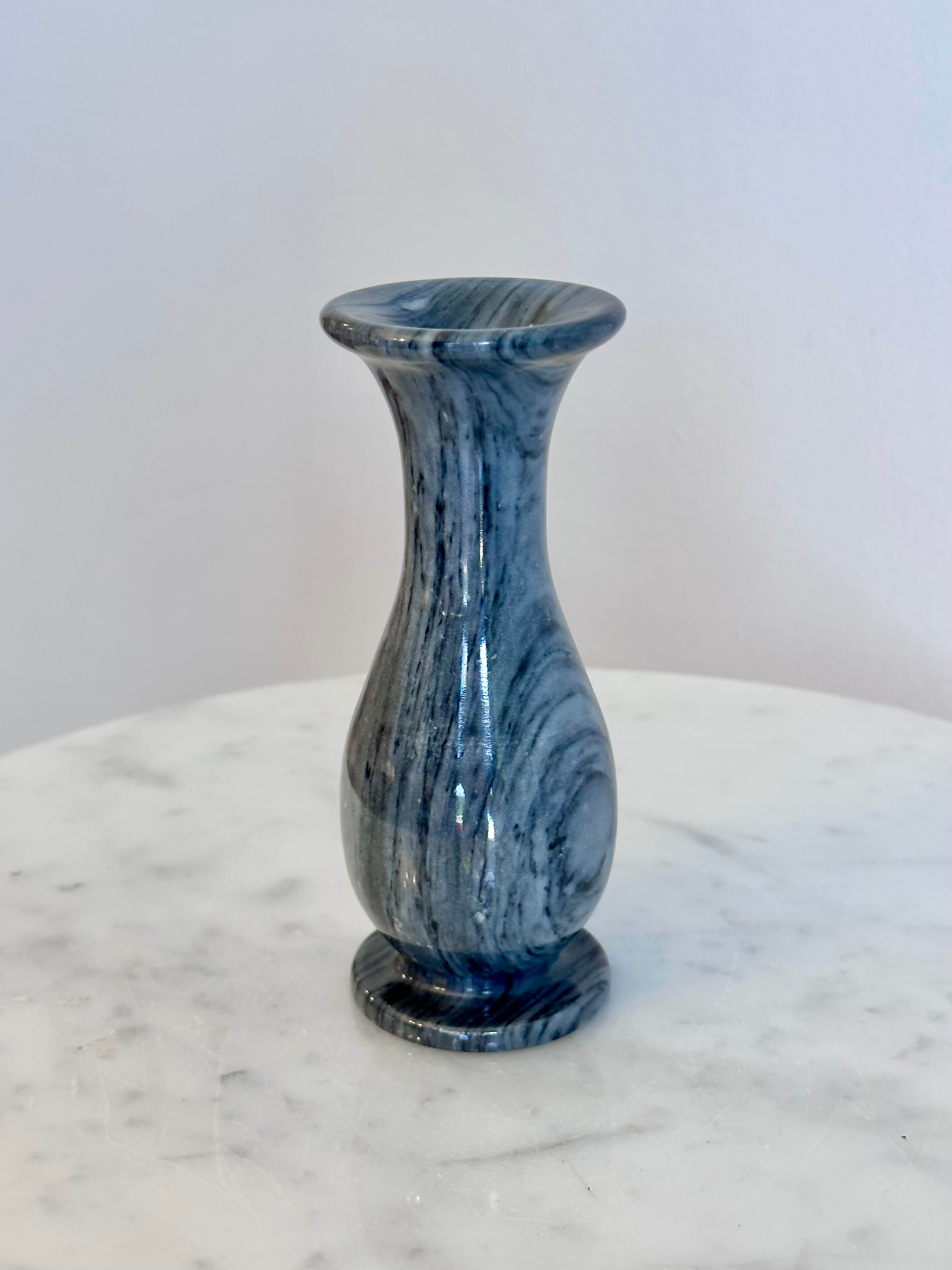 A small gray and white marbled stone vase with a flared rim and circular base, standing on a white marble surface against a plain off-white wall.