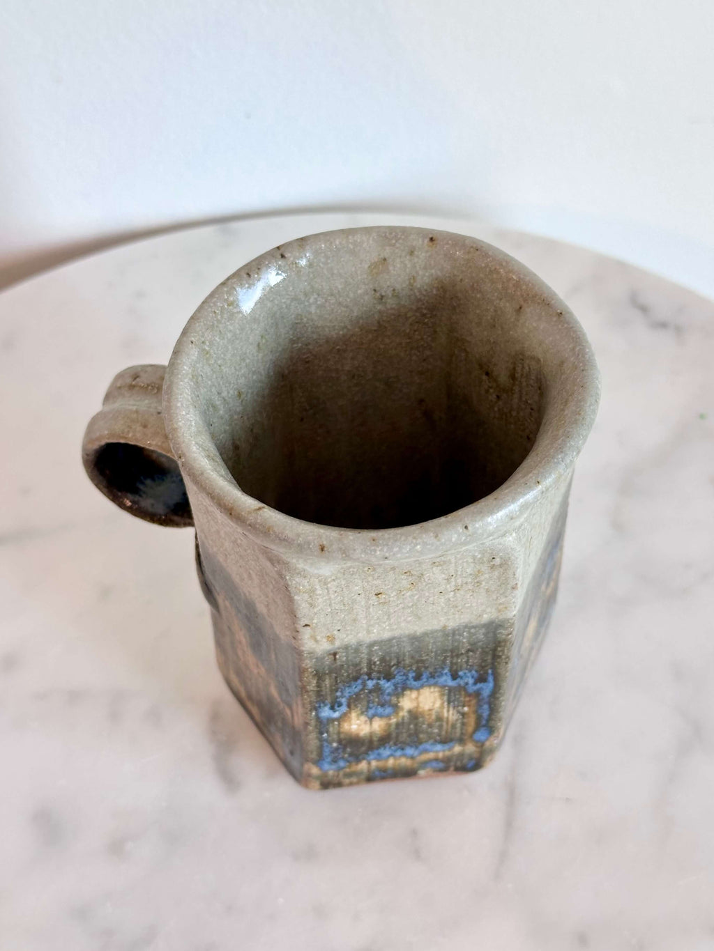 Top view of a handmade ceramic mug with a hexagonal body and a loop handle, featuring a layered glaze in gray, blue, and brown.