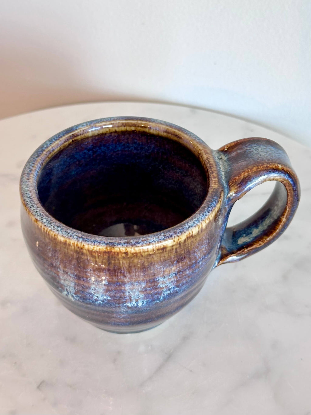 Top view of a handmade ceramic coffee mug with a blue purple drip glaze