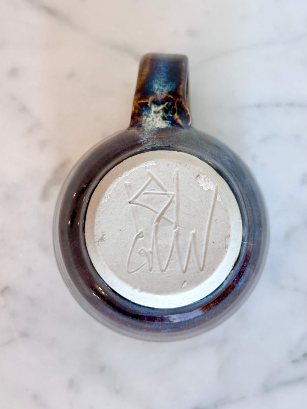 Bottom view of a handmade ceramic coffee mug with a blue purple drip glaze