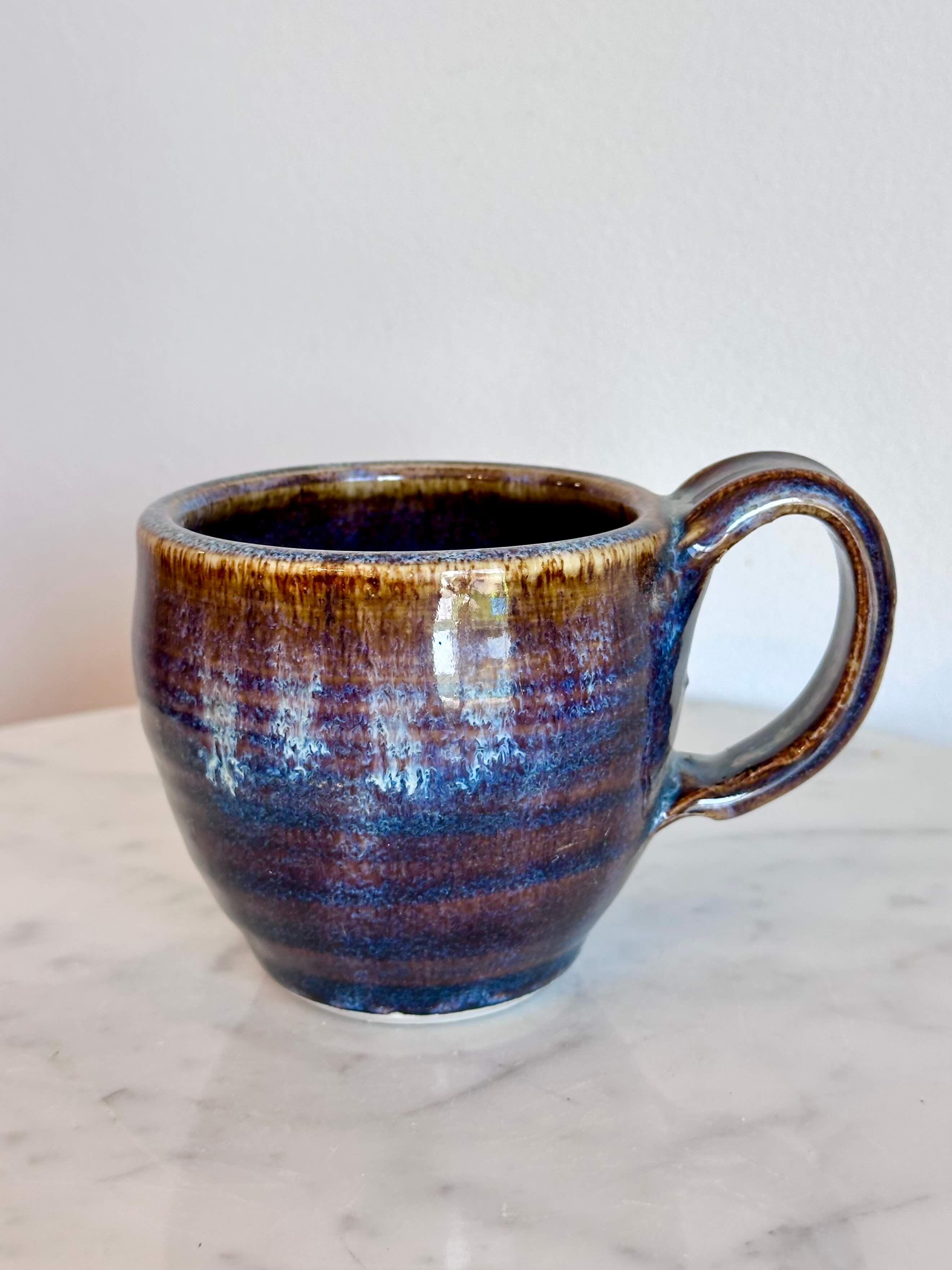 a handmade ceramic coffee mug with a blue purple drip glaze