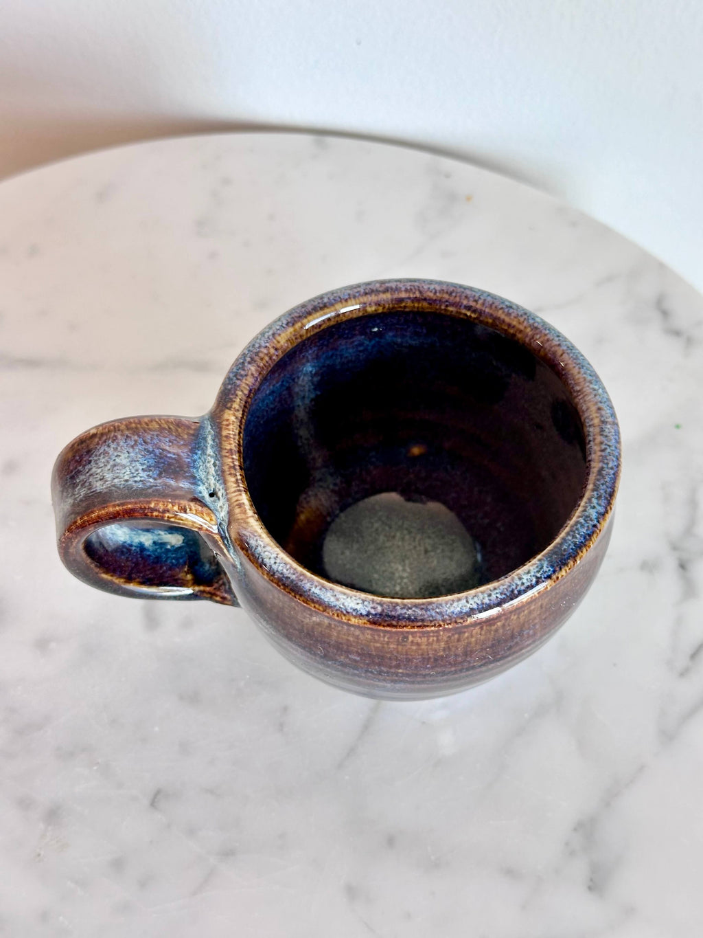 Top view of a handmade ceramic coffee mug with a blue purple drip glaze