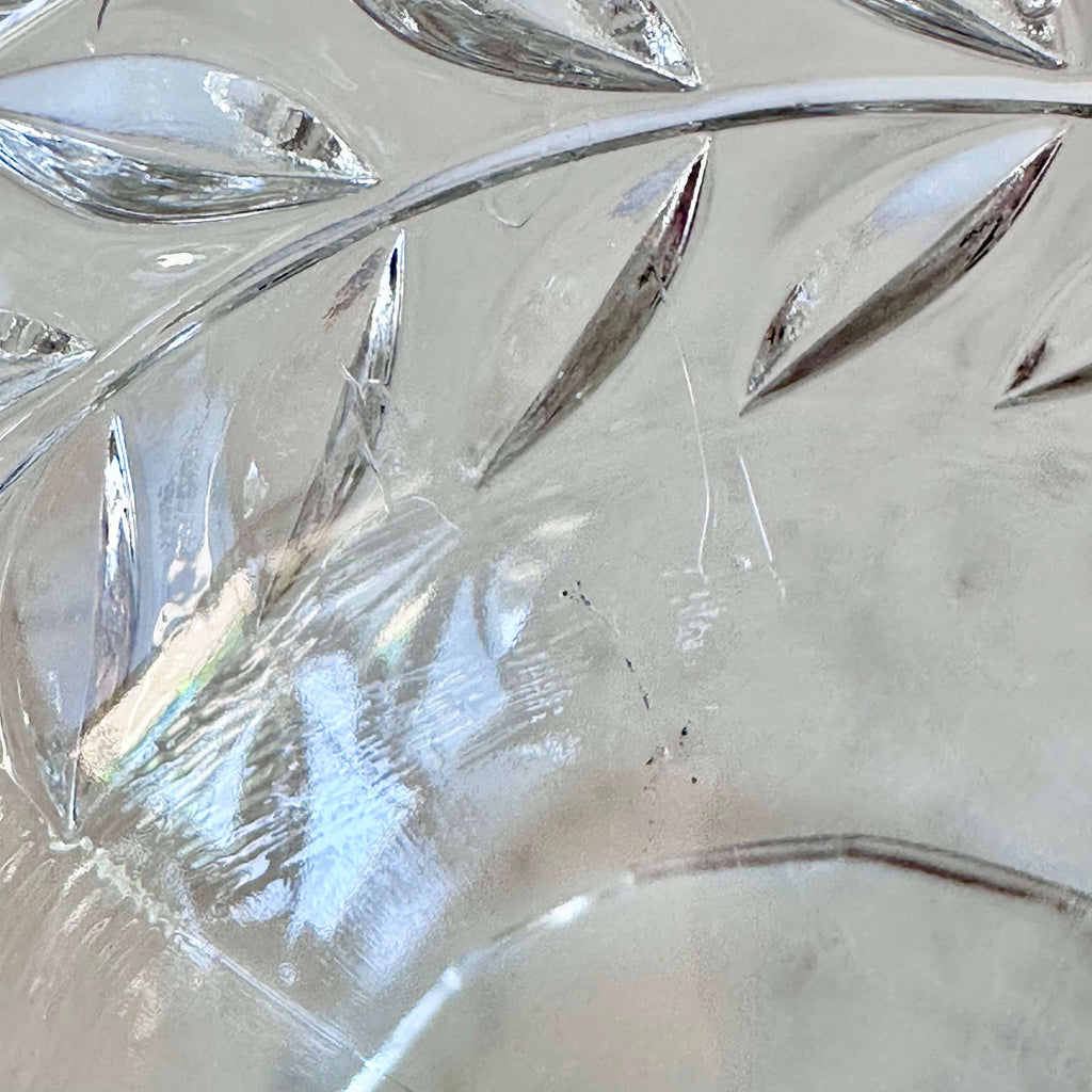 Close-up of a clear cut-glass bowl or dish with a leaf pattern, showing reflections and minor scuffs on the transparent surface.